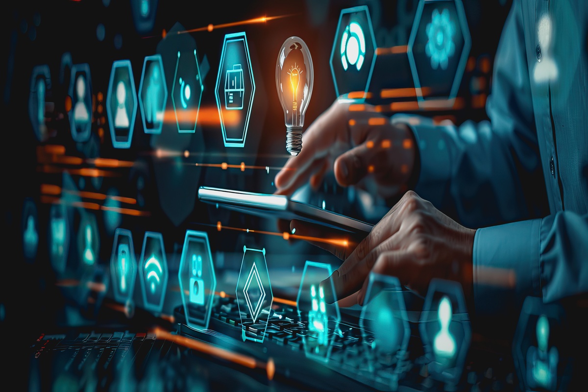 A person's hands using a tablet and keyboard, surrounded by a futuristic, glowing blue digital interface with hexagonal icons and a floating lightbulb graphic.
